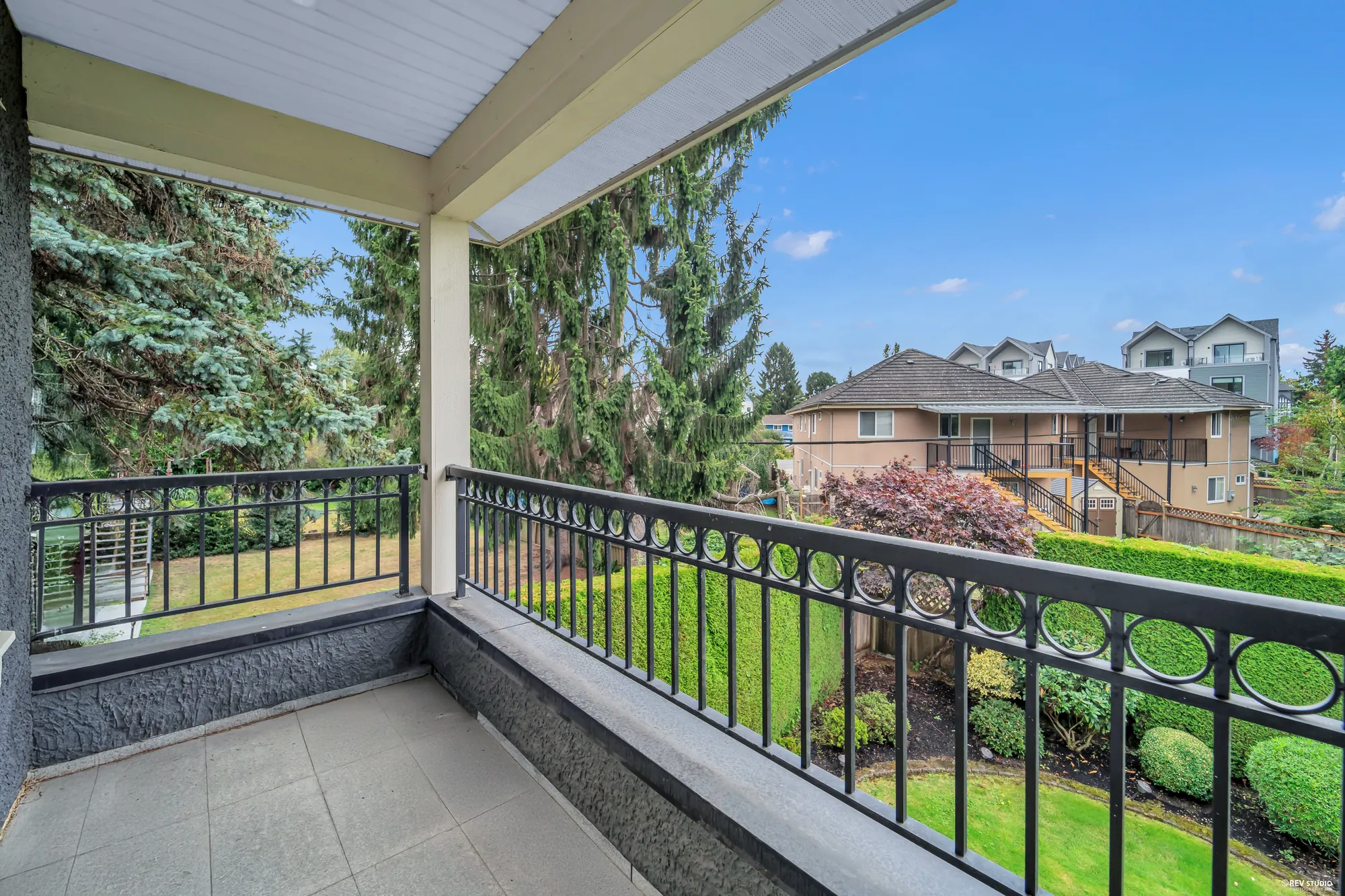 The covered balcony with its iron railing, over the lawn and hedge to the neighbours' roofs