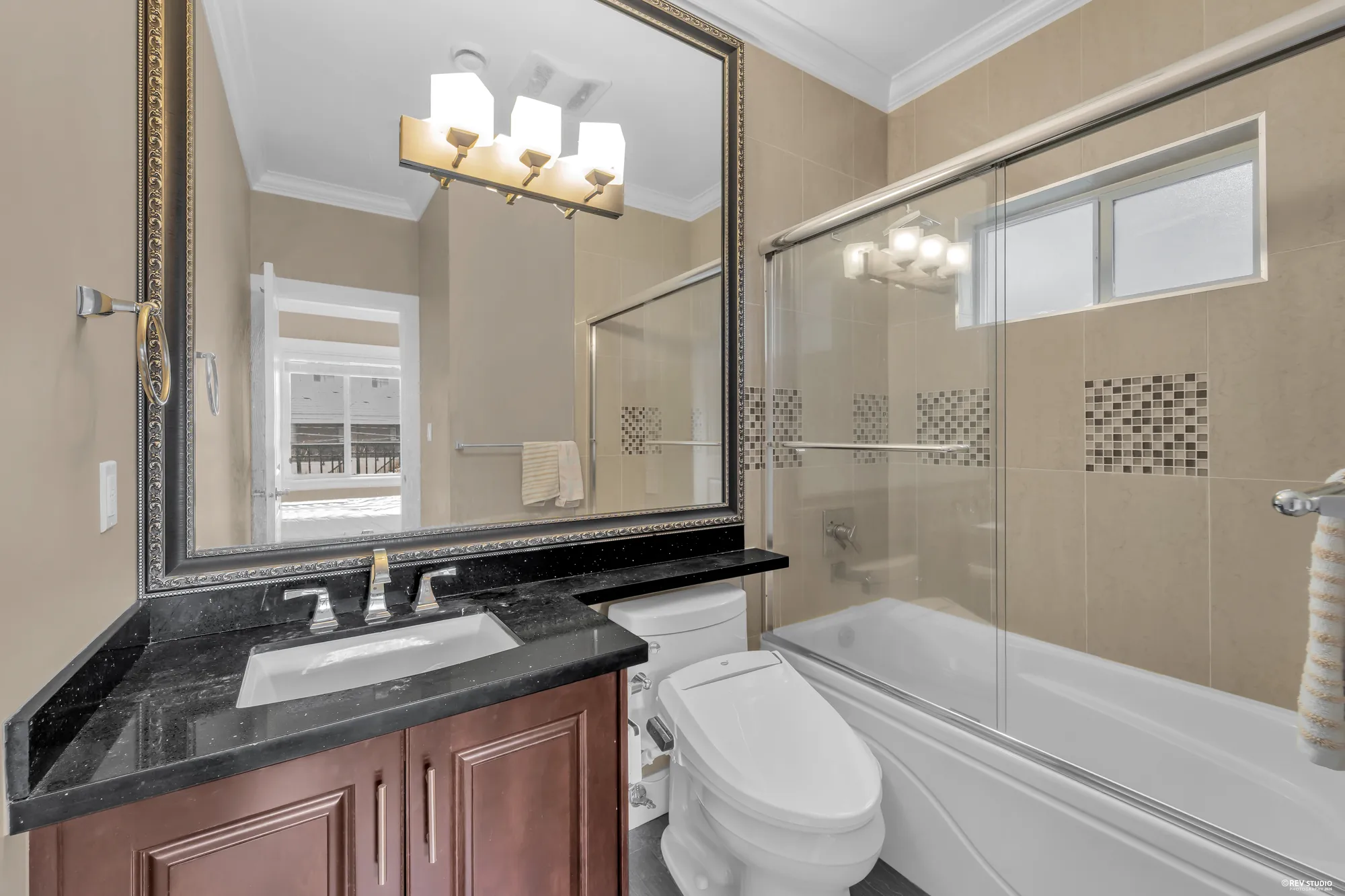 A bathroom with a tub and shower behind glass and a dark granite vanity