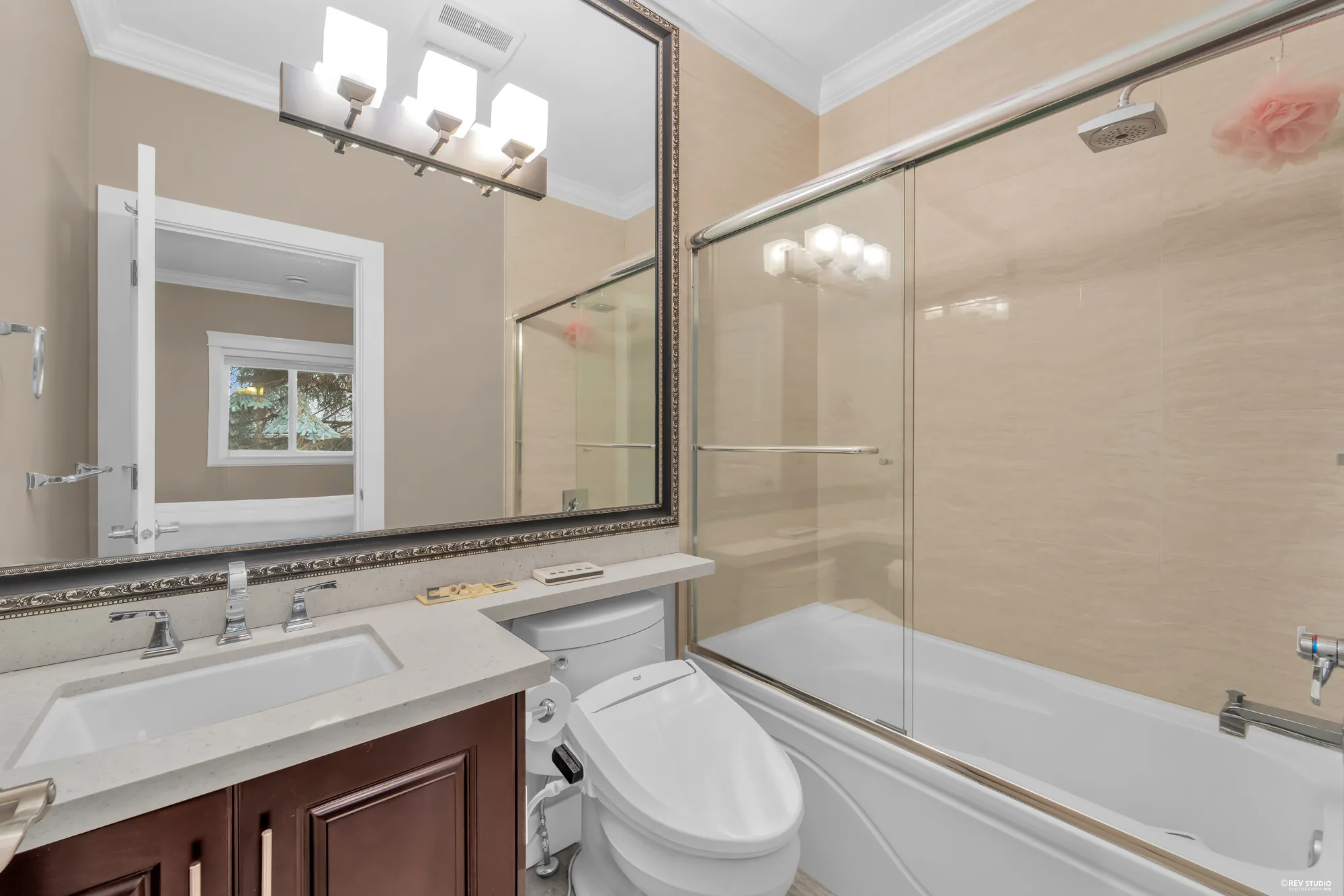 A bathroom with a tub and shower behind glass and a pale vanity