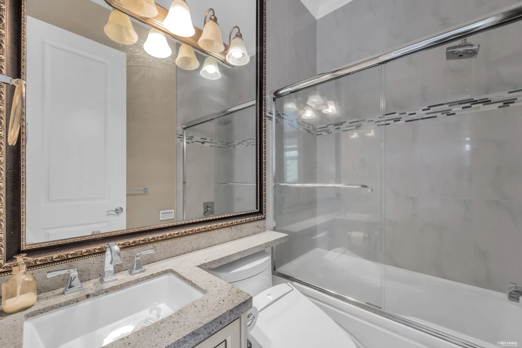 A bathroom with a tub and shower behind glass, a granite vanity