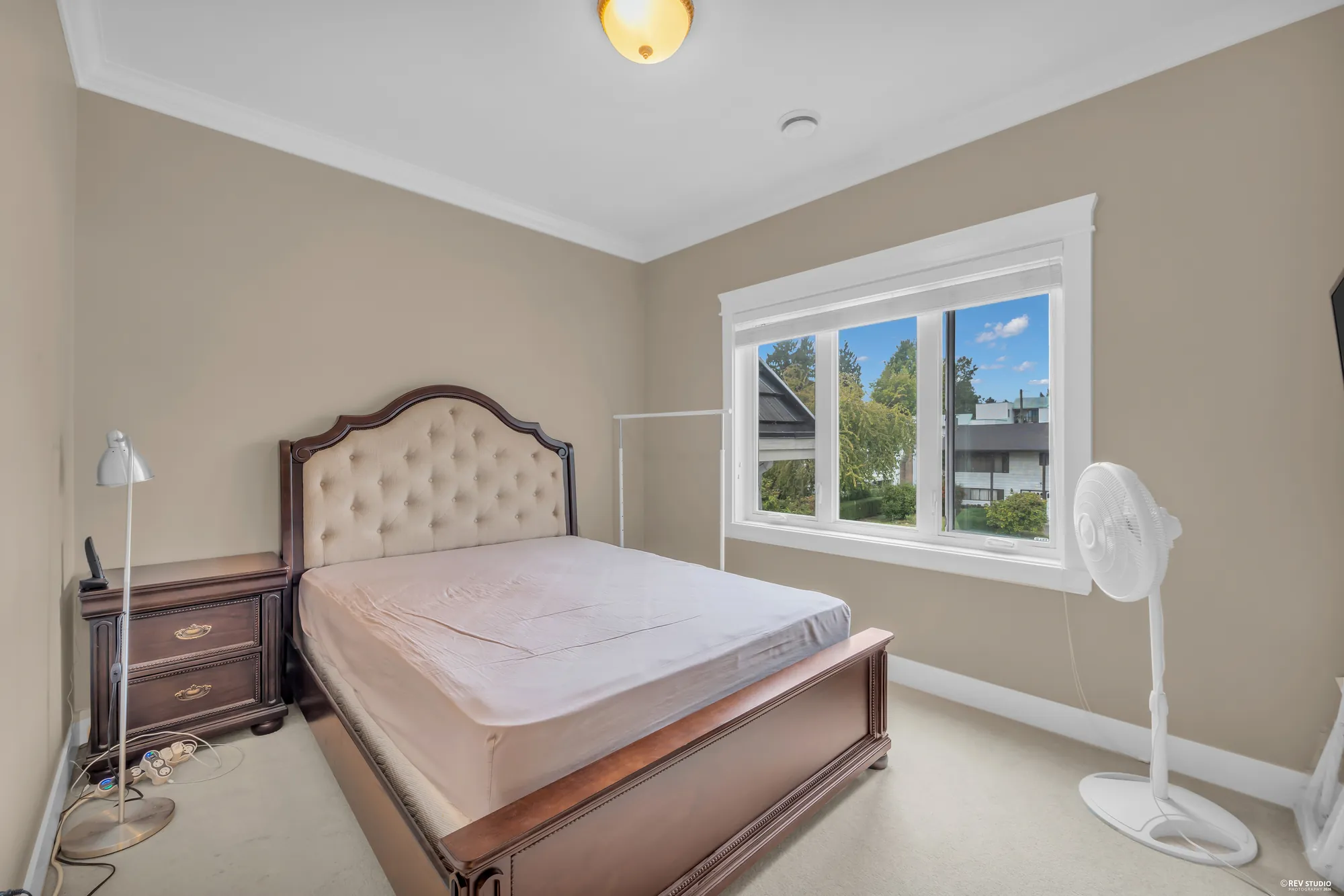 A bedroom with an upholstered bed by the window and a ceiling fan