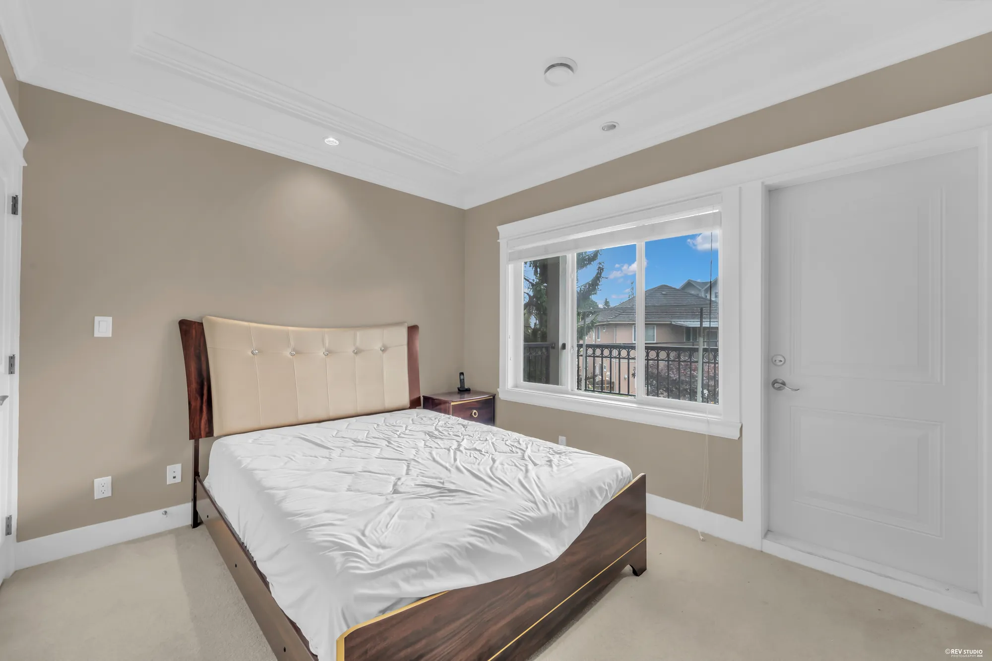 A bedroom with a bed by the window and a door to its bathroom