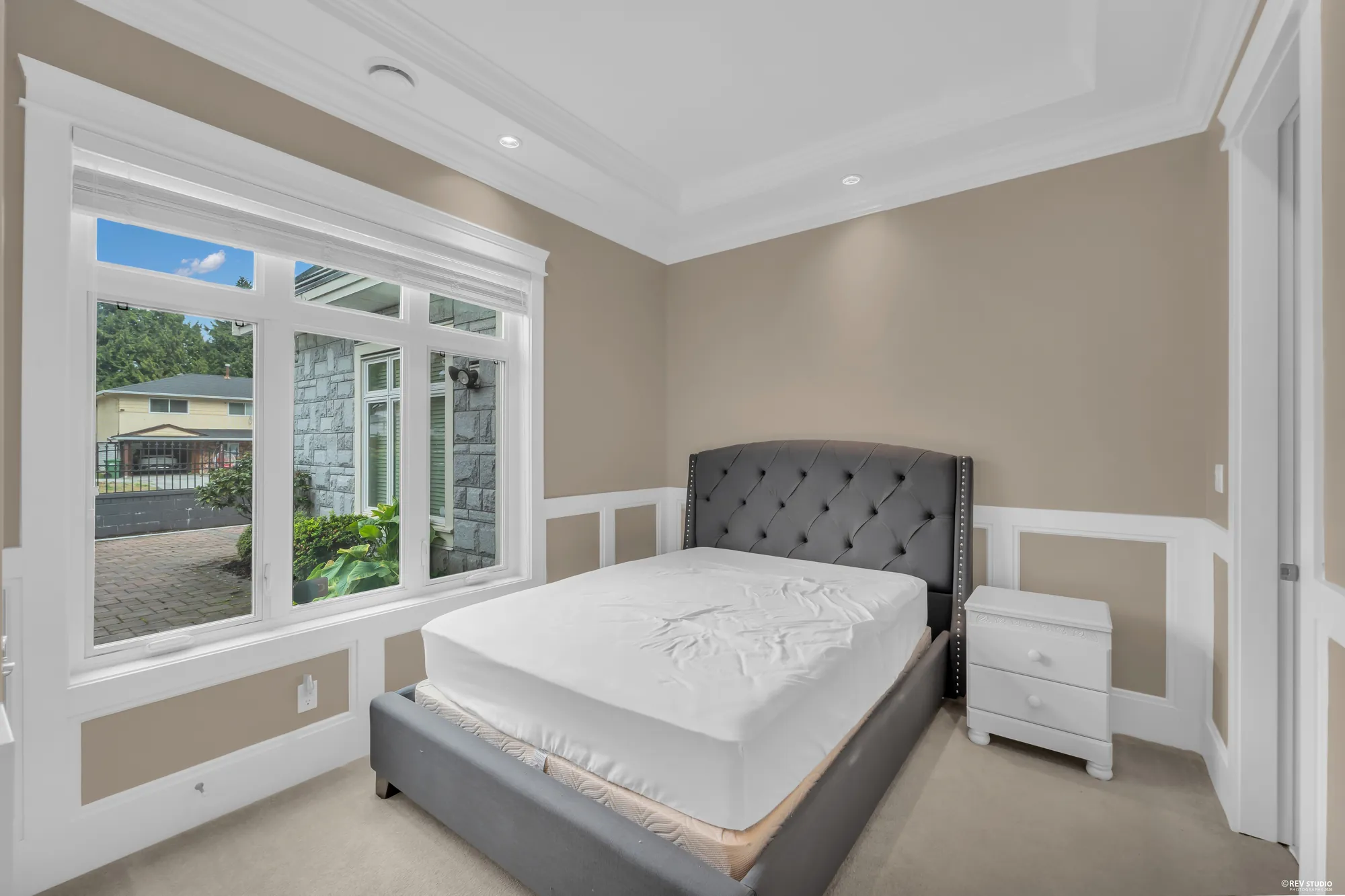 The main-floor bedroom: a grey upholstered bed under the window, panelled walls