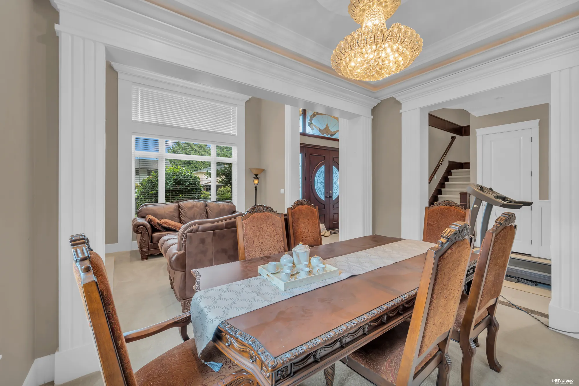 The dining room: a long table with upholstered chairs under a crystal chandelier, the front door beyond