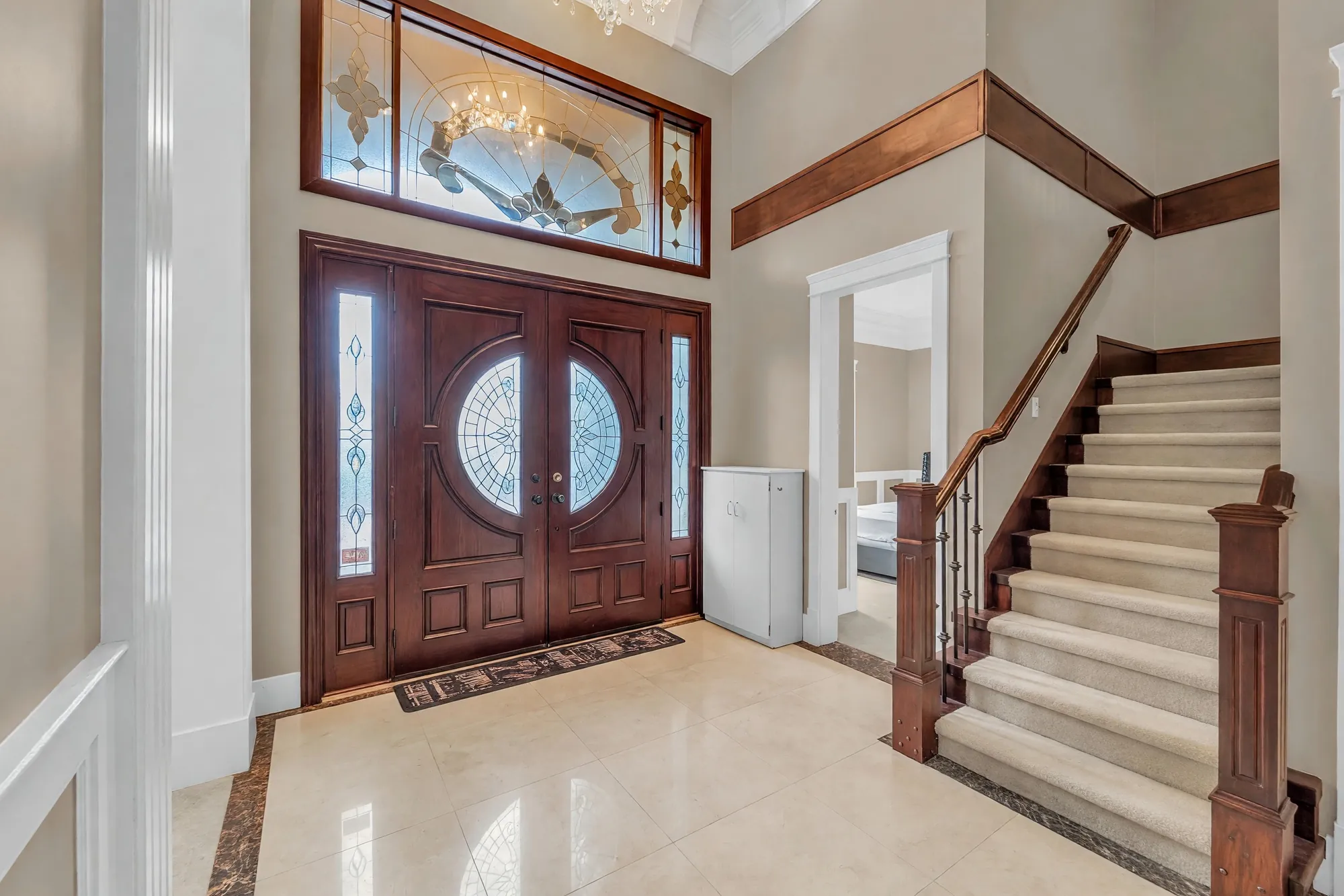 The foyer: the double front door with stained glass and a stained-glass transom, the carpeted stair with its dark rail