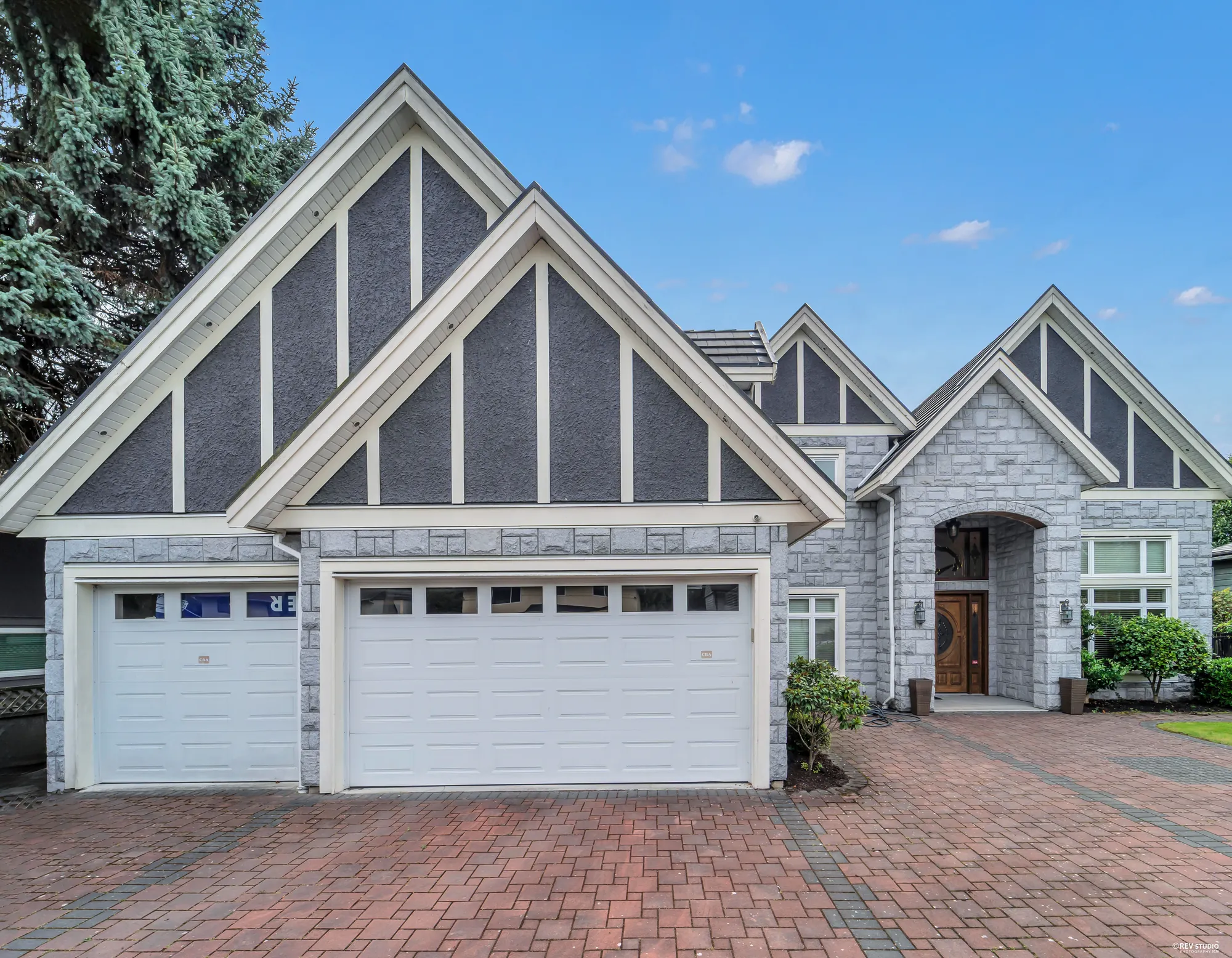 The two garage doors under their stone gable and the arched entry beside them, from the brick drive