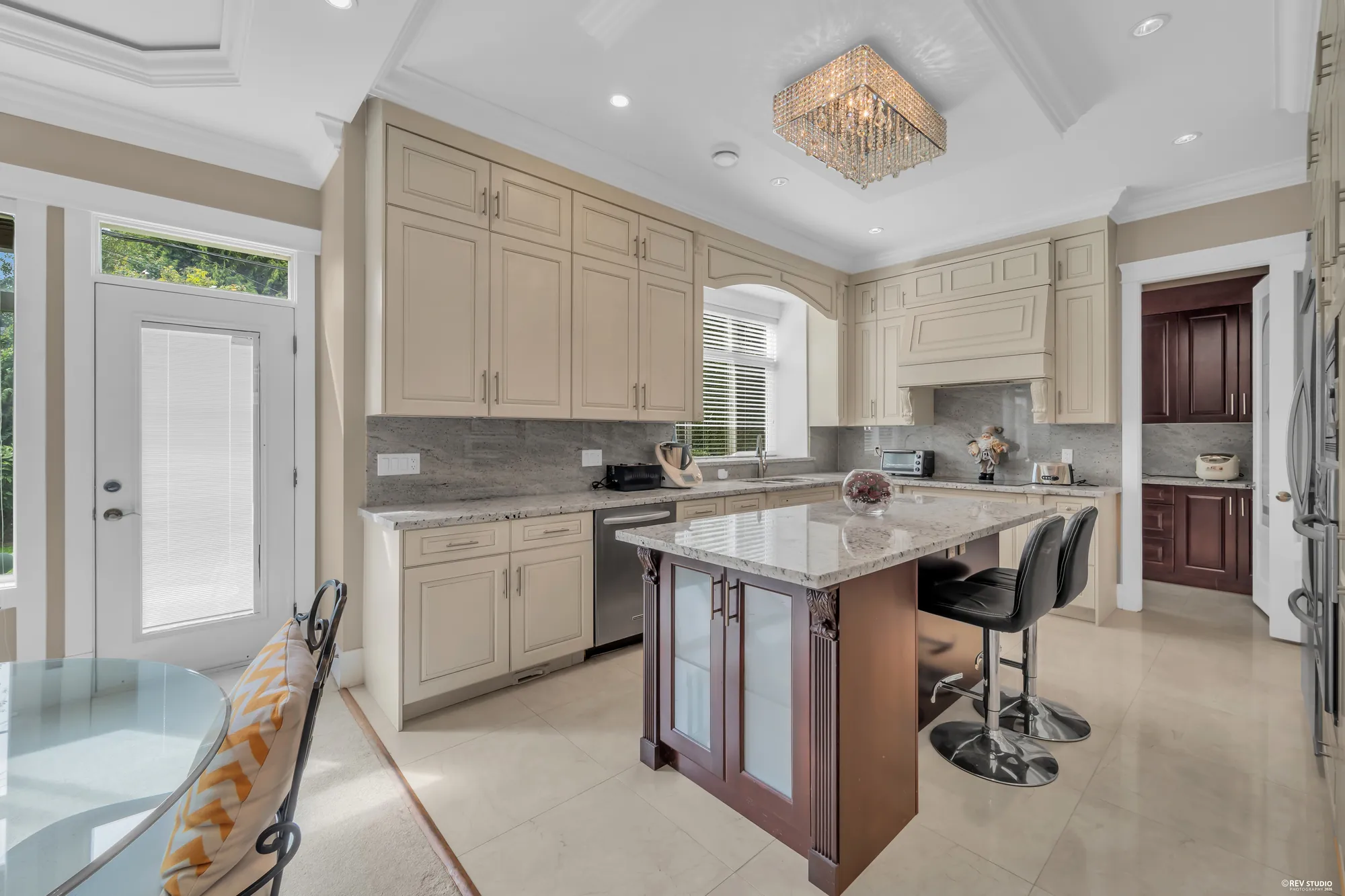 The kitchen: cream cabinetry, a granite island with a cherry base, a crystal ceiling fixture, the garden door at left