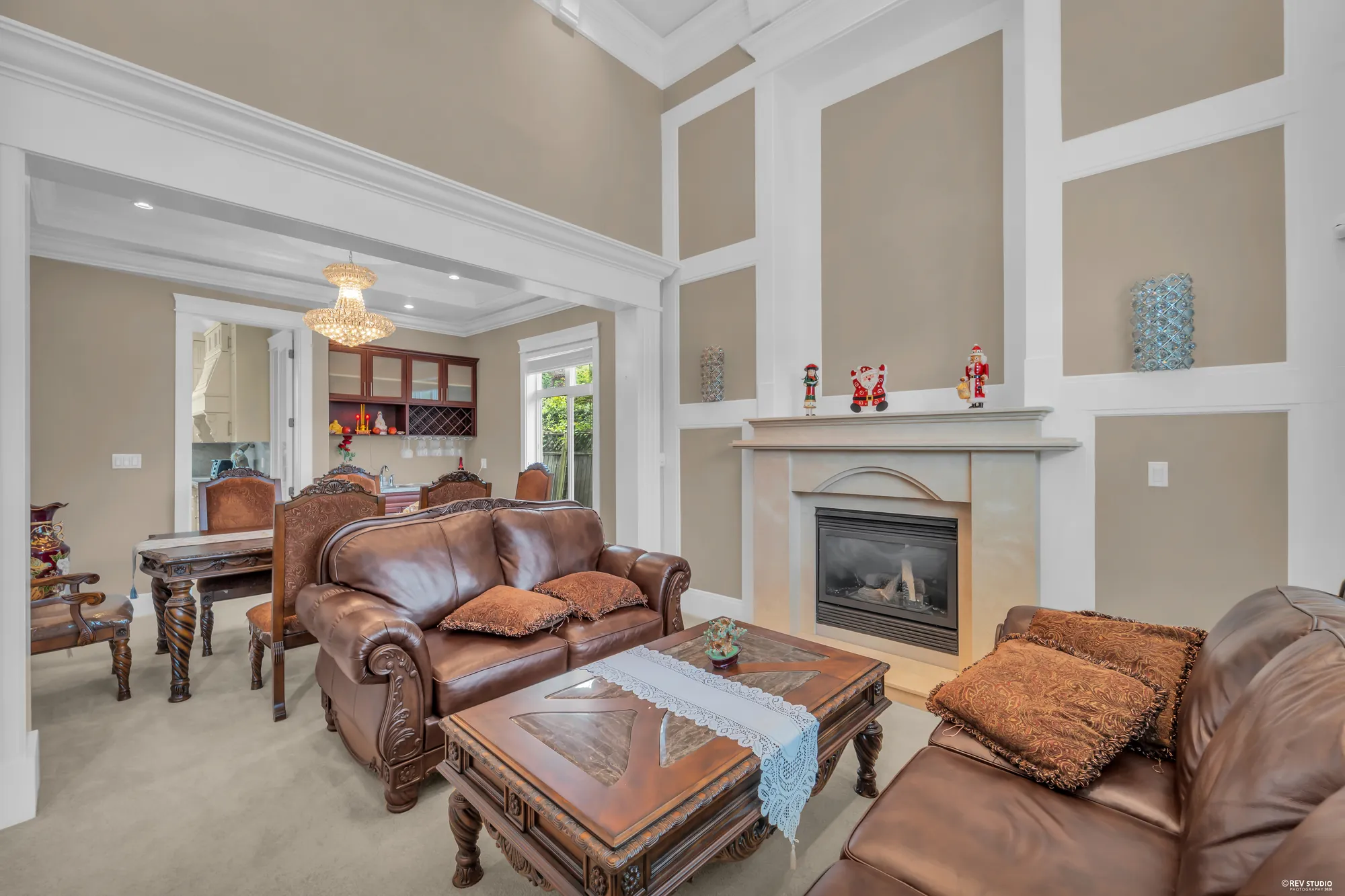 The living room open to the roof: a fireplace in a pale surround under panelled walls, leather sofas, a chandelier, the dining room beyond