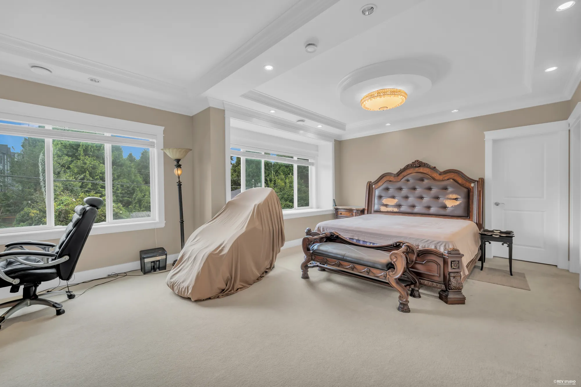 The primary bedroom: a carved bed under a tray ceiling with a crystal light, windows on two sides