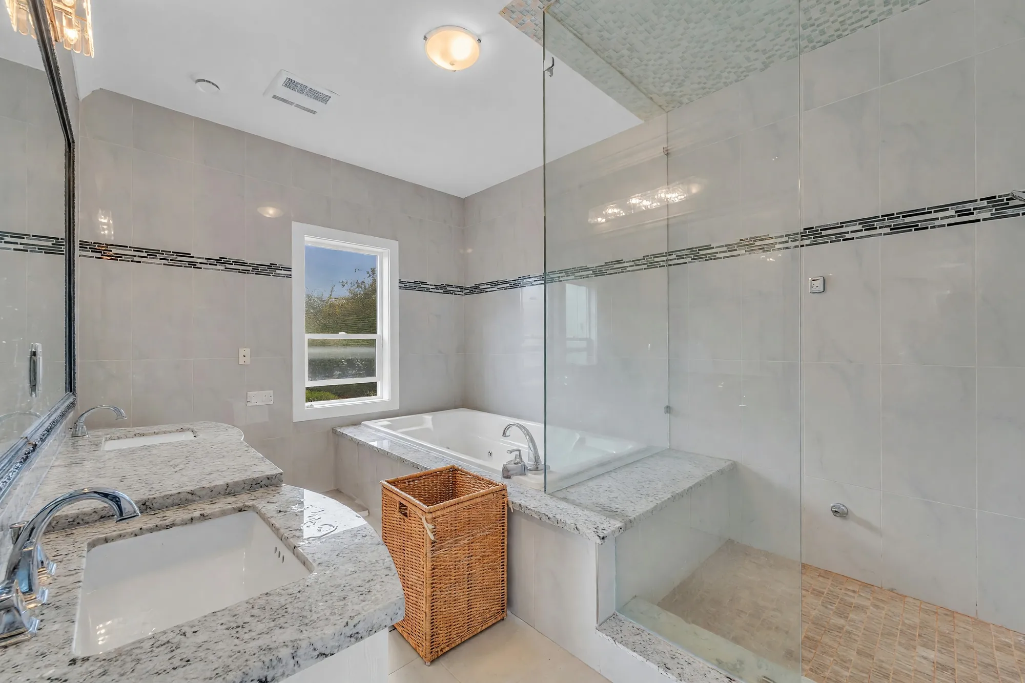 The primary bathroom: a tub under the window, a glass shower, marble-look tile