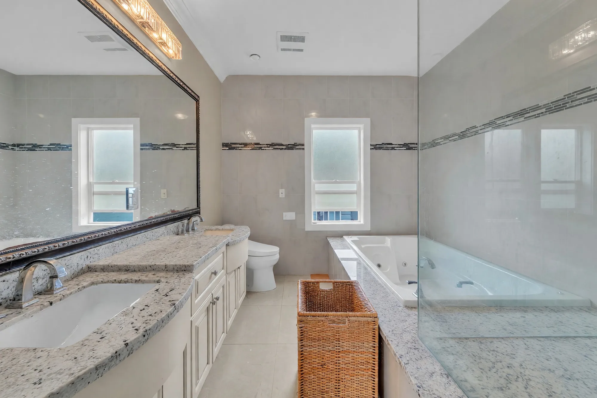 The long granite vanity of the primary bathroom under a wide mirror, the tub beyond