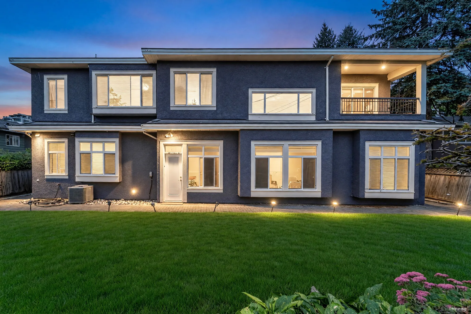 The same view of the back at dusk, the windows and the balcony lit
