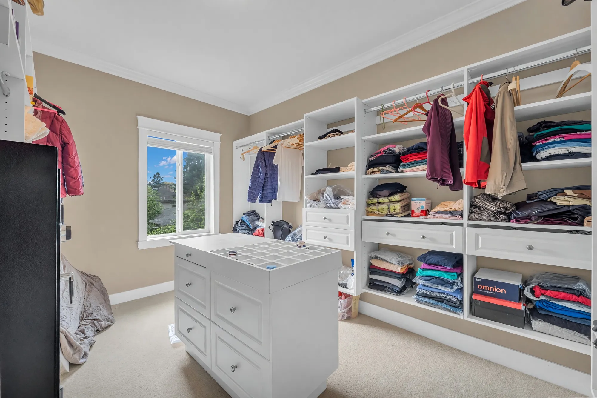 The walk-in closet: white shelving and rails on three walls, an island of drawers, a window